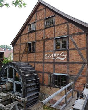 Vor dem dreigeschossigen Fachwerkhaus befindet sich ein Mühlrad aus Holz. Das Gebäude trägt das Logo des Museums.