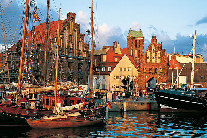 Der Hafen von Wismar ist in ein goldenes Sonnenuntergangslicht getaucht, welches die roten Backsteinfassaden betont.  