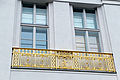 Eine Nahaufnahme der zwei Doppelfenster im Mittelrisaliten über dem Haupteingang des Landeshauptarchives zeigt ein dekoratives Geländer mit goldenen Verzierungen vor diesen Fenstern.  