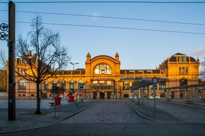 Das Bahnhofsgebäude in der Frontansicht hat einen Vorplatz mit Bushaltestellen. Der mittlere Pavillon der Empfangshalle ist durch zwei niedrigere Zwischenglieder mit zwei Eckpavillons verbunden. Die Ziegelfassade besteht aus gelben Klinkern, die im Abendlicht leuchten. 